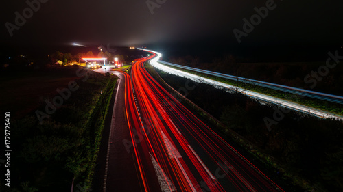 Highway traffic light trails at night with gas station
