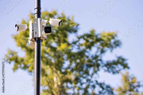 Security camera system mounted on a pole, featuring multiple lenses and sensors, surrounded by lush greenery, capturing surveillance footage in an outdoor environment