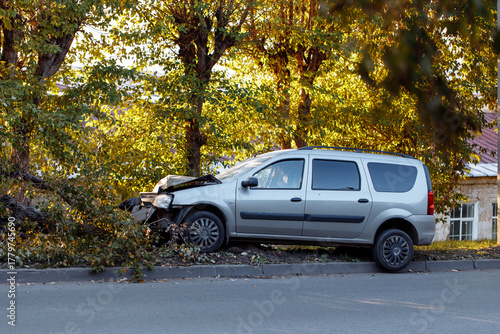 Road traffic accident.A silver car damaged in the accident stands against the background of trees on the side of the road, demonstrating the consequences of the collision.