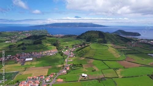 AZORES - 10.27.2025 - Great aerial footage traveling over Faial Island's green hills, headed towards the water with a view of a Pico Island volcano in the distance.