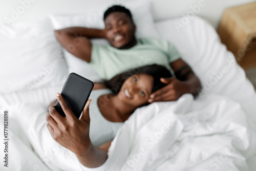 Billede på lærred In a bright room, a couple relaxes in bed, wrapped in white sheets