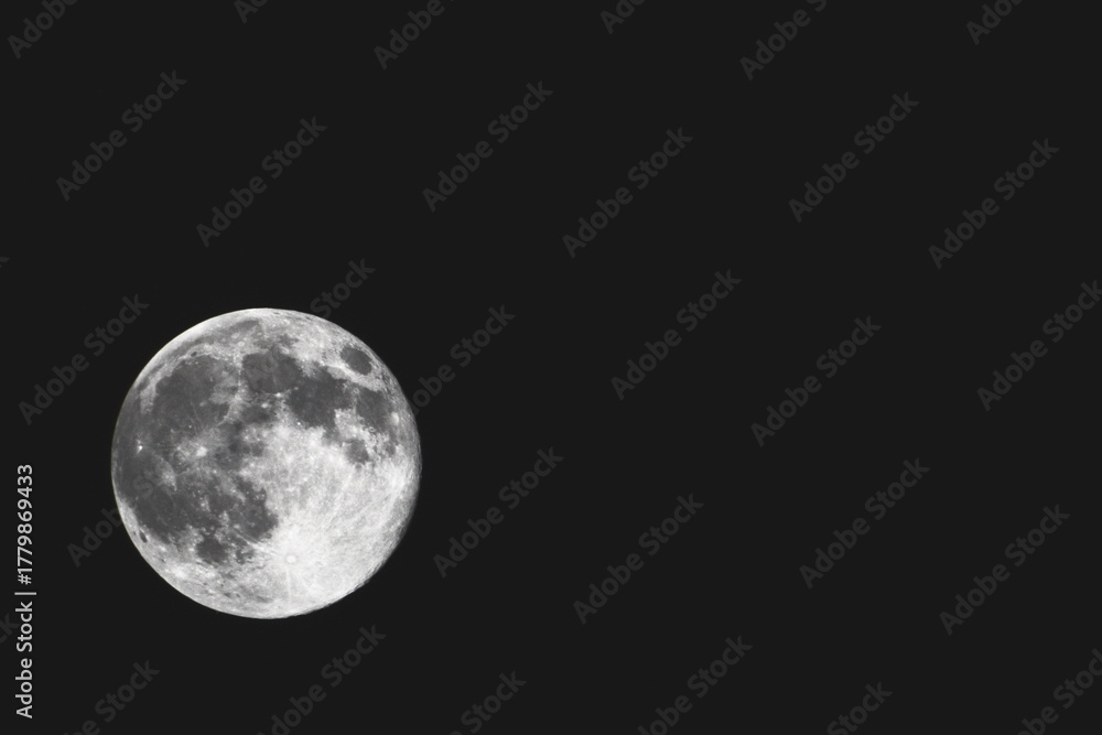 Obraz premium Close-up black and white photograph of the full moon against a dark night sky, showing detailed craters and surface texture.