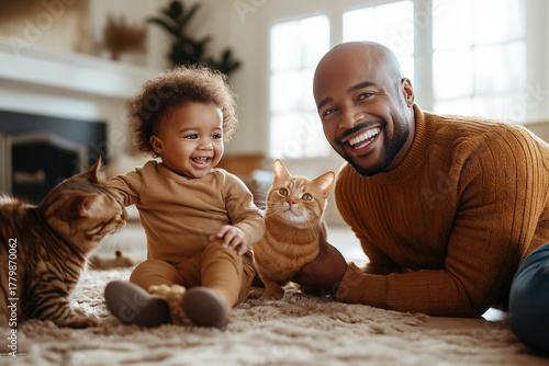 Father and baby play with cats in the living room. They smile as the cats interact nearby.