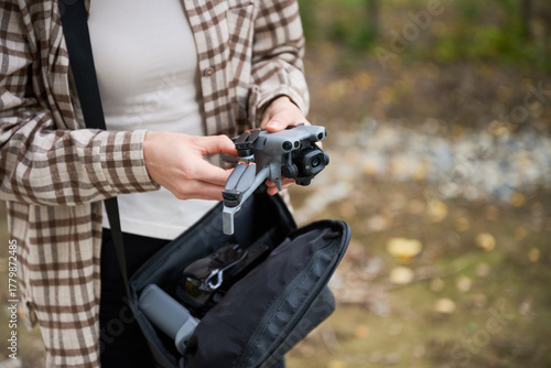 A person stands in a natural setting, carefully taking a drone from a bag, excited for the aerial exploration ahead.