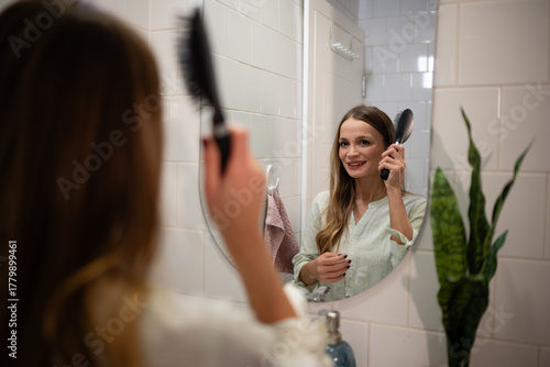 Woman brushing hair in bathroom mirror reflection