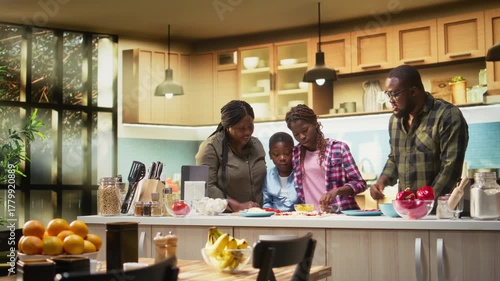 African American parents and kids sharing pizza day at home, adding mozzarella over the dough with multiple ingredients. Togetherness, laughter, family bonding and homemade cooking. Camera A.