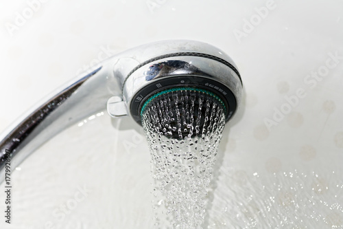 Stream of Water Flowing from Modern Chrome Shower Head on White Tiles