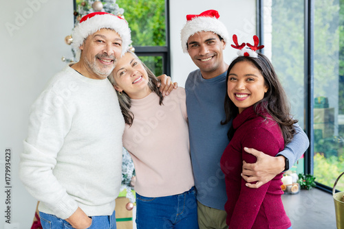 Diverse couples wearing cozy sweaters and Santa hats celebrating in living room with Christmas tree
