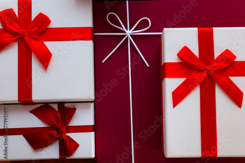 stylish gift packaging featuring satin bows on dark background, chic holiday gift boxes adorned with red ribbons arranged artfully on deep crimson surface