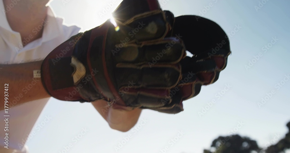 Fototapeta premium Holding padded glove toward camera on sports field, showing white polo sleeve and sun halo