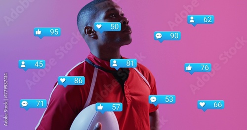Holding white football, red jersey athlete with black tee posing in pink studio with blue icons