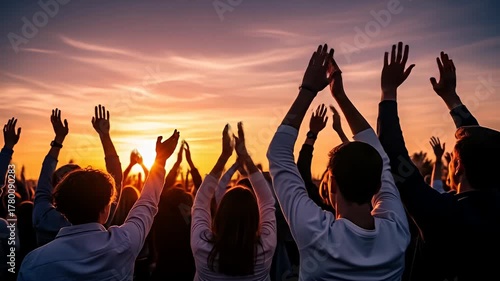 Crowd raises hands against fiery sunset, conveying unity and celebration