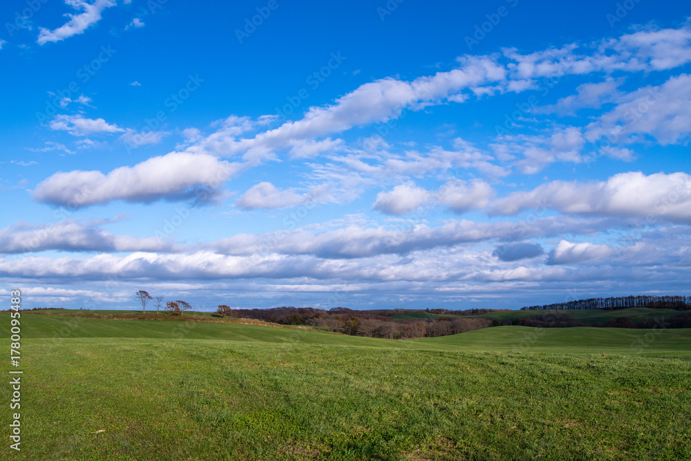 Fototapeta premium A gentle stretch of green hills under a blue sky with clouds