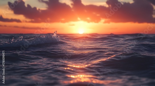 A vibrant sunset casts an orange glow on the waves of the ocean as the sun begins to set.