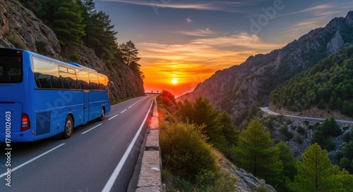 Obraz na płótnie A blue bus driving down a winding mountain road at sunset.