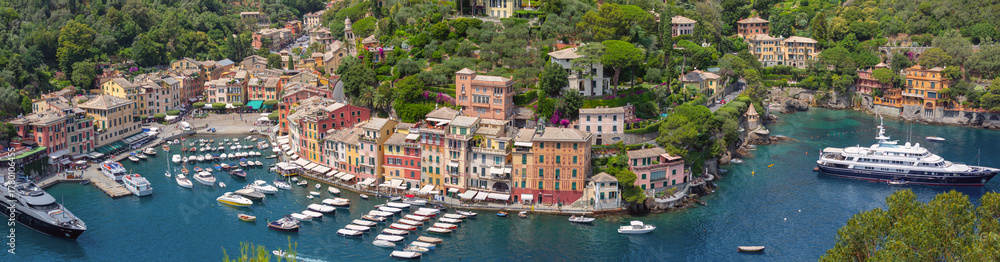 Obraz premium Panoramic photo of Portofino harbor with boats, buildings and green hills in Italy, Liguria region
