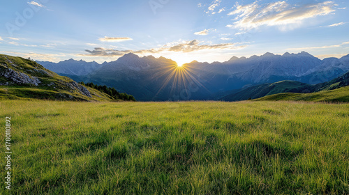 Fototapeta Naklejka Na Ścianę i Meble -  Golden sunlight illuminates vast green meadow with majestic mountains in background