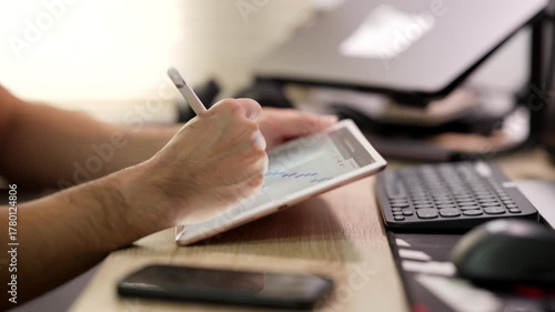A person uses a stylus on a tablet showing financial charts while typing on a keyboard in an office.