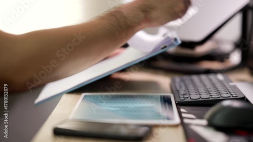 A person uses a stylus on a tablet while reviewing documents and working at a computer in an office setting.