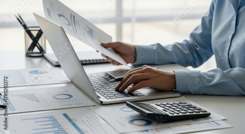 Financial report analysis tax budget financial accounting specialist reviews printed charts desk while entering data laptop and calculator showing focused planning and organized office workflow