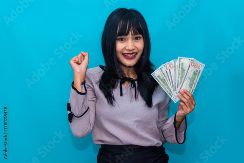 Smiling proudly, the woman celebrates her success while holding a handful of dollar bills. Ideal for income, entrepreneurship, and business growth.