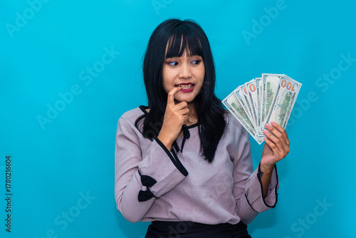 A thoughtful woman holds money near her lips, looking curious and pleased. Ideal for finance, savings, and investment visuals.