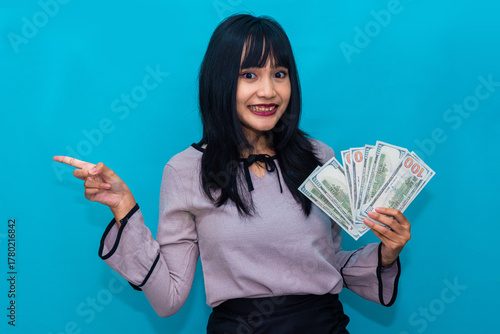 A happy woman points toward her money with joy, showing achievement and enthusiasm. Ideal for promotions, finance blogs, and savings campaigns.