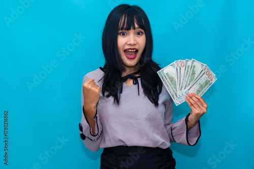 A joyful woman raises her fist while holding a fan of dollar bills, expressing success and excitement. Ideal for finance, rewards, and business victory visuals.