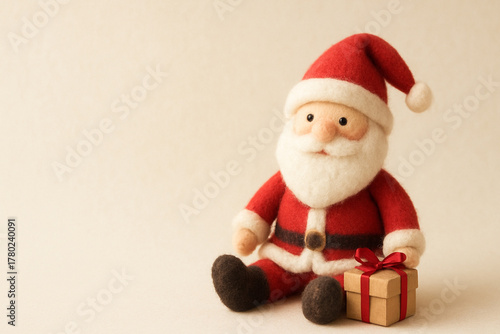 A vintage-style felt Santa Claus toy sitting cheerfully, with a small gift box next to him. Textured background in a warm cream color, perfectly clean for text. The feeling is heartwarming.