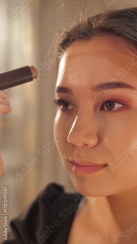 A young woman applies makeup in front of a mirror, focusing on her daily beauty and skincare routine. Elegant and natural look, perfect for beauty, lifestyle, and cosmetic content.