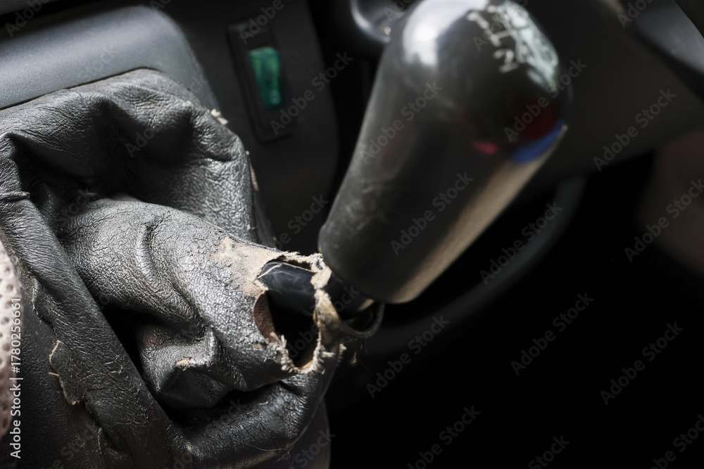 Obraz premium Close up view of worn, torn, and damaged car gear stick inside an old vehicle interior. broken lever and obsolete gaiter show clear signs of neglect and decay