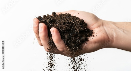 A hand holds a clump of dark soil some spilling down set against a white background