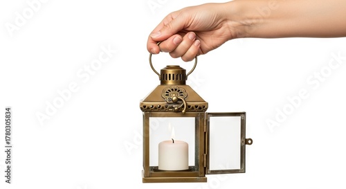 A hand holds a lit candle in a brass lantern with an open door against a white background