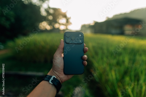 New smartphone in hand, green blurred background of rice fields in nature