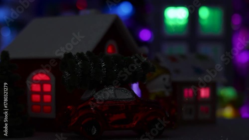 A small Christmas village with decorated houses illuminated by flashing lights rotates against the backdrop of a large town