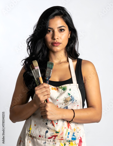 artist wearing a paint-splattered apron holding brushes, creative pose on white background