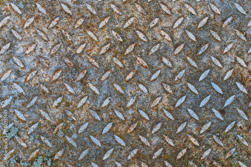 The surface of an old, worn sheet metal with a lentil-shaped ribbing. There are spots of old gray paint and rust. Background. Texture. Close-up.