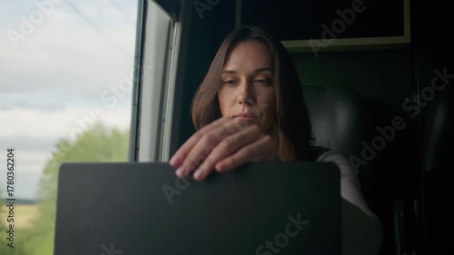 Woman focused on laptop while traveling through scenic countryside on a train