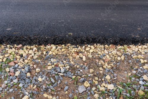 A close-up of the edge of a new black asphalt road on a bed of crushed stone and sand. Background.