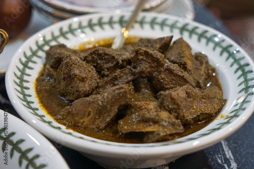A bowl of rendang hati lembu (beef liver rendang) in thick, dark gravy served in a patterned ceramic bowl with spoon, isolated on white background.