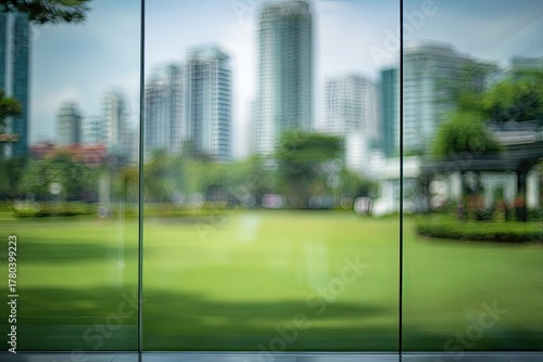 Blurred view of city park through glass walls.  Urban park scene, softened by glass.  Cityscape seen in soft focus.?Green lawn, trees, buildings in background