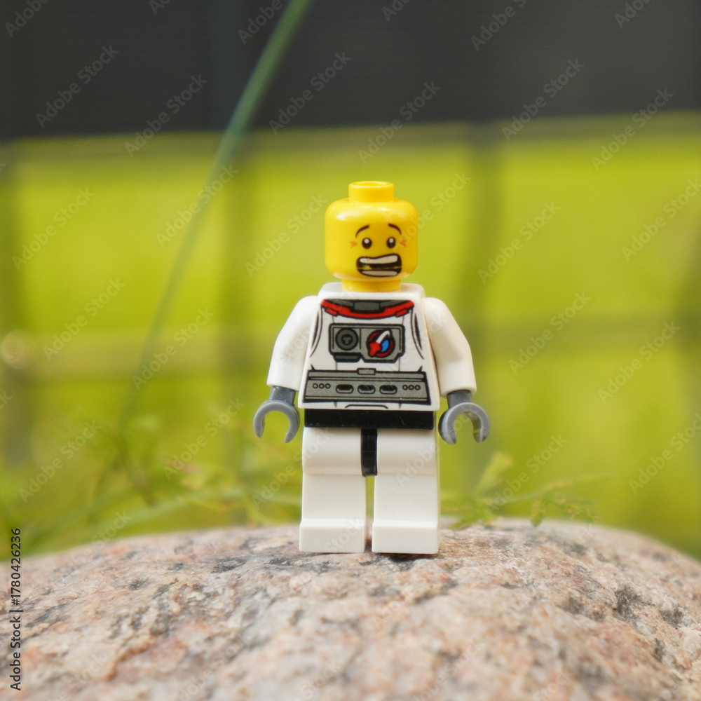 Fototapeta premium Lego astronaut figure standing on a rock with a blurred green background