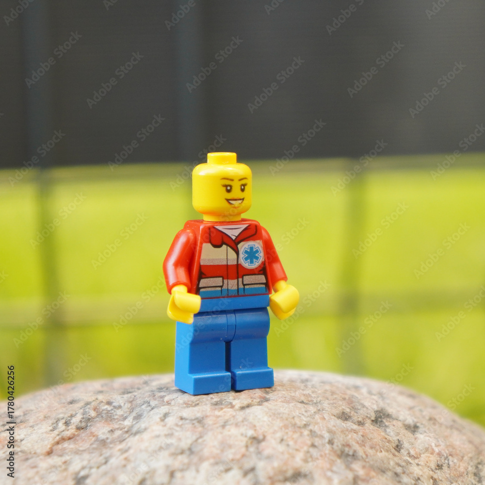 Naklejka premium Lego paramedic minifigure standing on a rock with a blurred green background