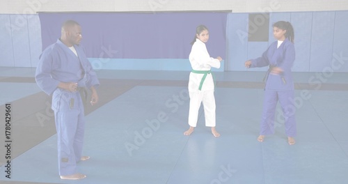 Directing instructor in blue gi guiding students sparring in dojo on foam mats, with colored belts