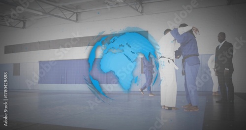 Grappling pair of martial artists practicing judo on blue mats at gymnasium, with digital globe