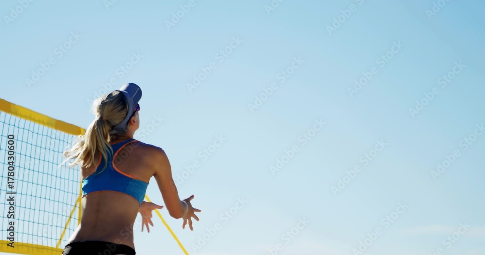 Obraz premium Preparing beach volleyball player raising arms near yellow net, wearing blue sports bra, copy space