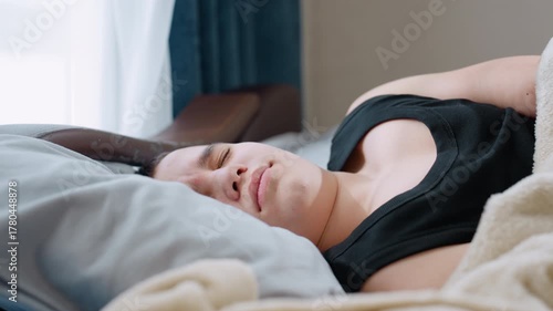Close up boy in black singlet sleeping on pillow looking restless with closed eyes showing discomfort and uneasy rest under blanket in bedroom highlighting tired child