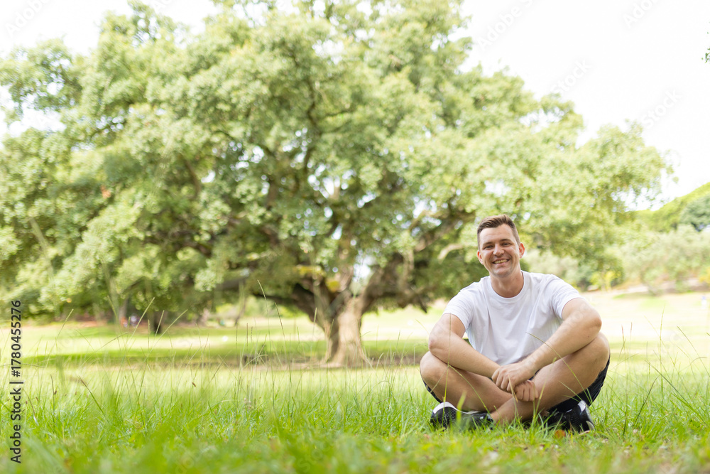 Obraz premium Man smiling, relaxing outdoors on grass in a park
