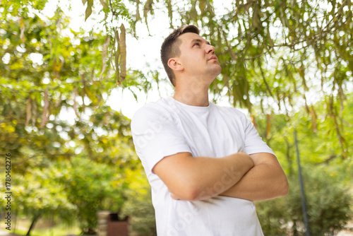 Young man standing outdoors contemplating future with arms crossed