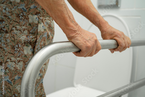 Asian elderly woman patient use toilet support rail in bathroom.